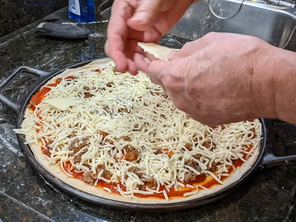 Adding cheeses to pizza on pizza cast iron pan
