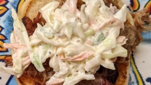 adding coleslaw topping to pulled pork sandwich