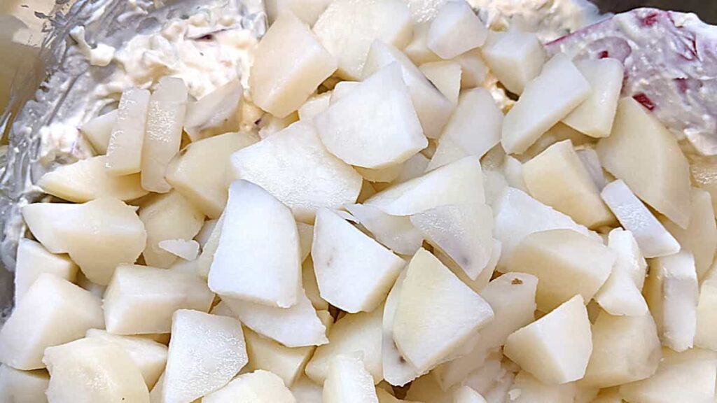 adding cooked potatoes on top of other mixed ingredients for how to make southern potato salad