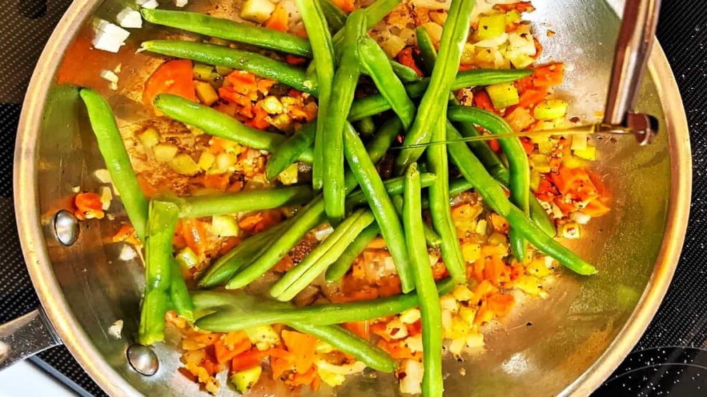 adding green beans and oil to veggies skillet for potatoes with green beans recipe