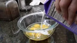 adding half and half cream into eggs for scrambled eggs recipe in stainless steel pan