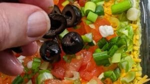adding layer 7 of sliced black olives to 7 layer dip recipe