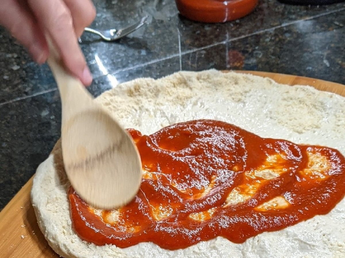 Adding sauce to sausage and pepperoni pizza