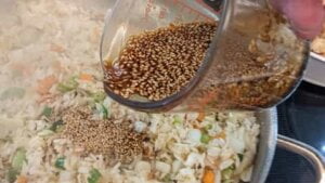 adding seasoning solution to veggies rice mixture for asian chicken rice casserole