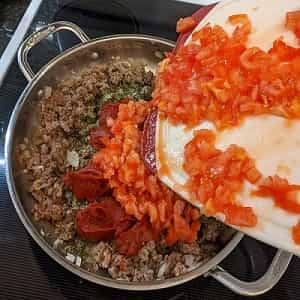 adding tomatoes to browned meat for lasagna meat sauce