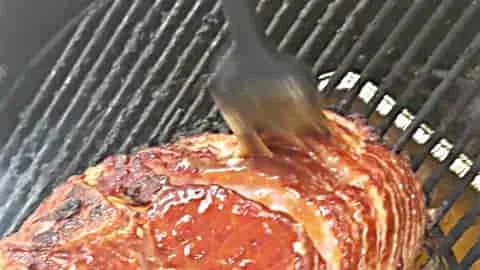 applying ham glaze to spiral ham on the grill