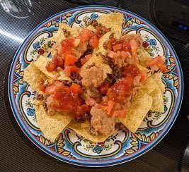 Building ground beef nachos by adding tomatoes and salsa