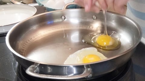 cracking eggs into hot pan of oil for making sunny side up eggs in stainless steel cracking eggs into hot pan of oil for making sunny side up eggs in stainless steel