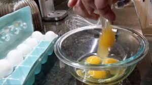 cracking eggs into mixing bowl for scrambled eggs recipe in stainless steel