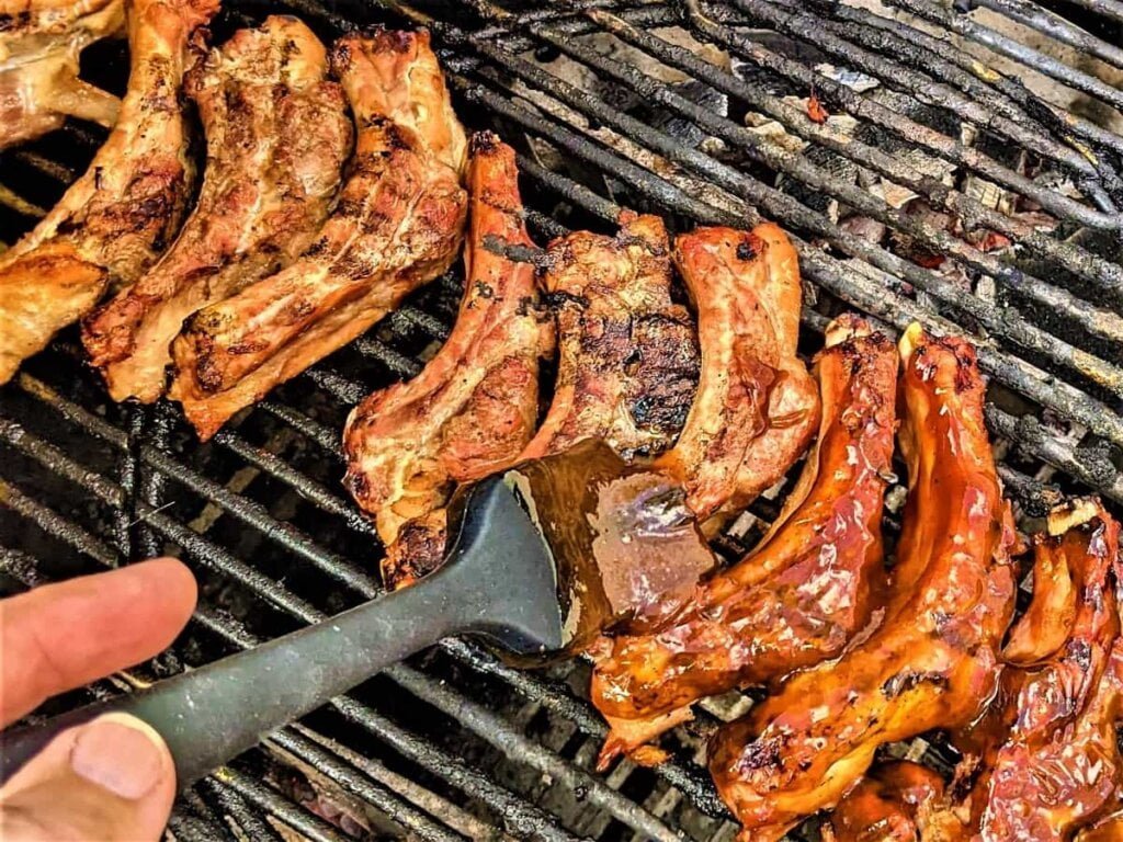 Grilling ribs and brushing bbq sauce while grilling on charcoal