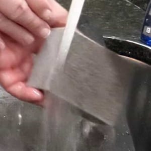 how to clean pizza steel showing rinsing off pumice stone cleaning brick