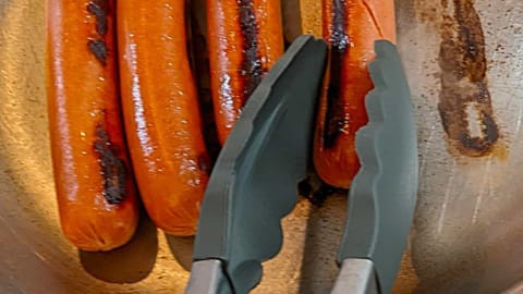 pan frying hot dogs while searing and rolling them over pan frying hot dogs while searing and rolling them over
