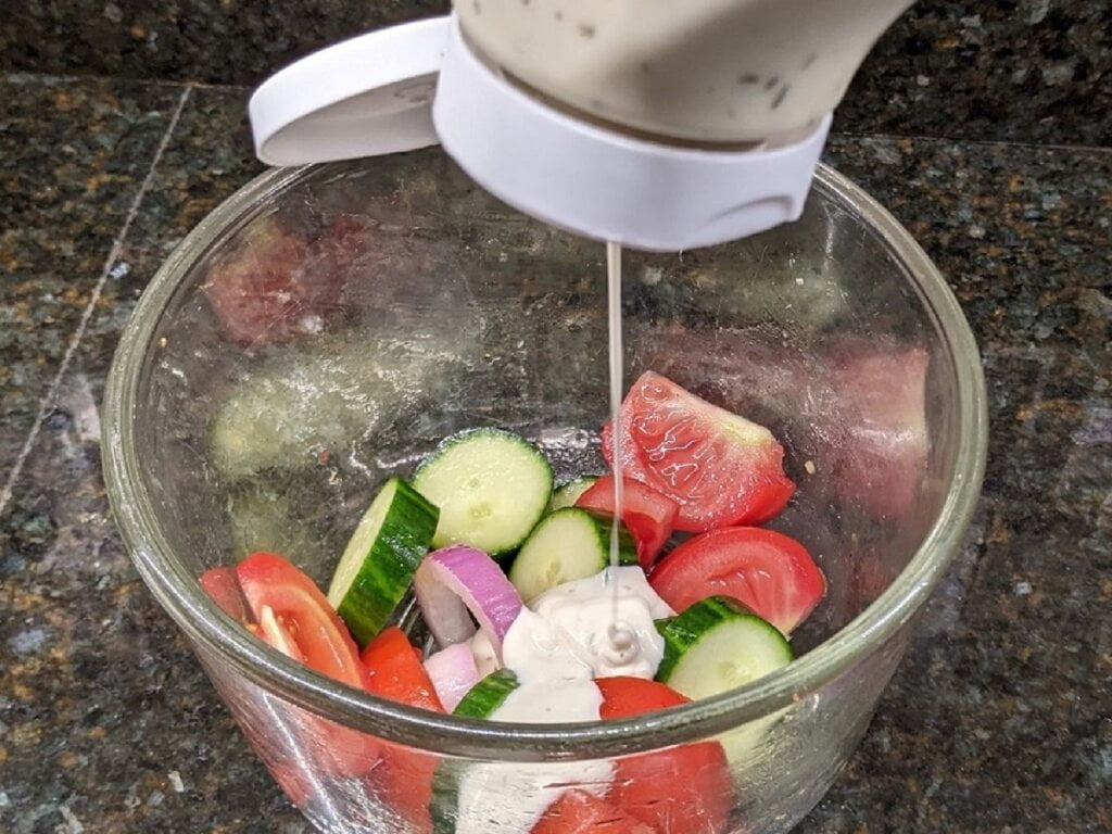 Pouring dressing for cucumber tomato salad with ranch dressing