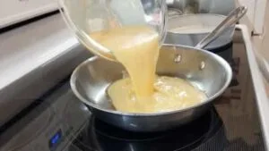 pouring egg mixture into hot oiled stainless steel pan for scrambled eggs recipes