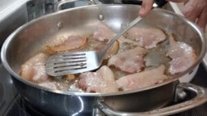 pressing down curled parts of frying bacon on stovetop