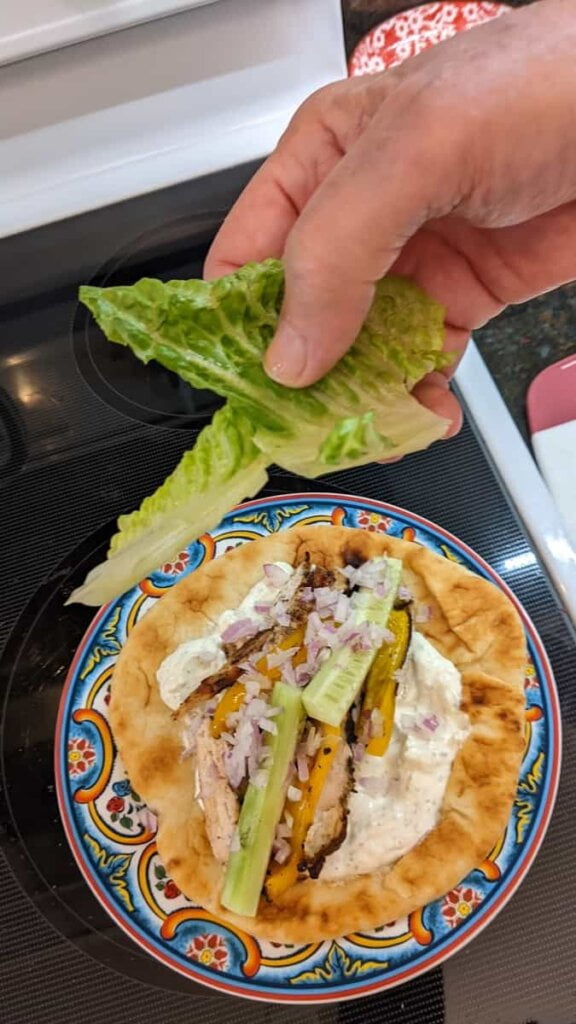 putting toppings on sandwich for gyro chicken recipe