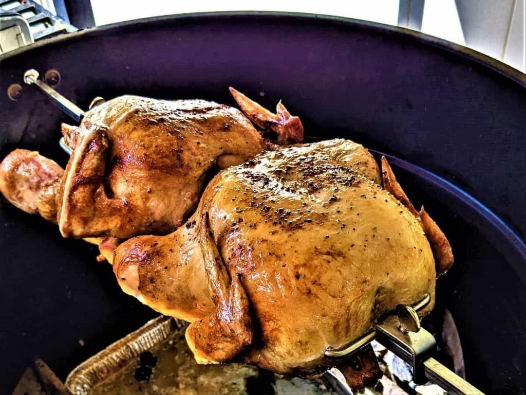 Rotisserie of 2 chickens grilling on charcoal