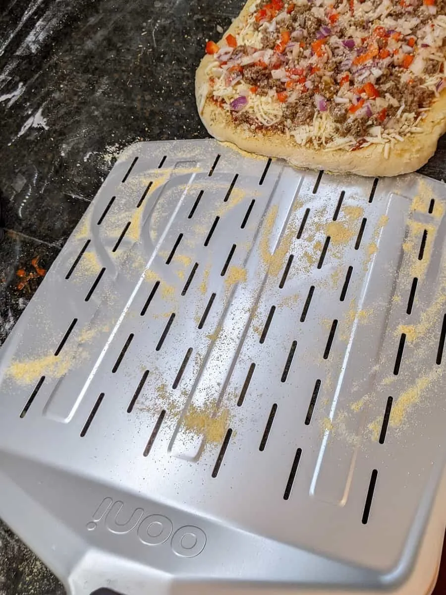 scooping up pizza from counter with metal peel for transfer to oven