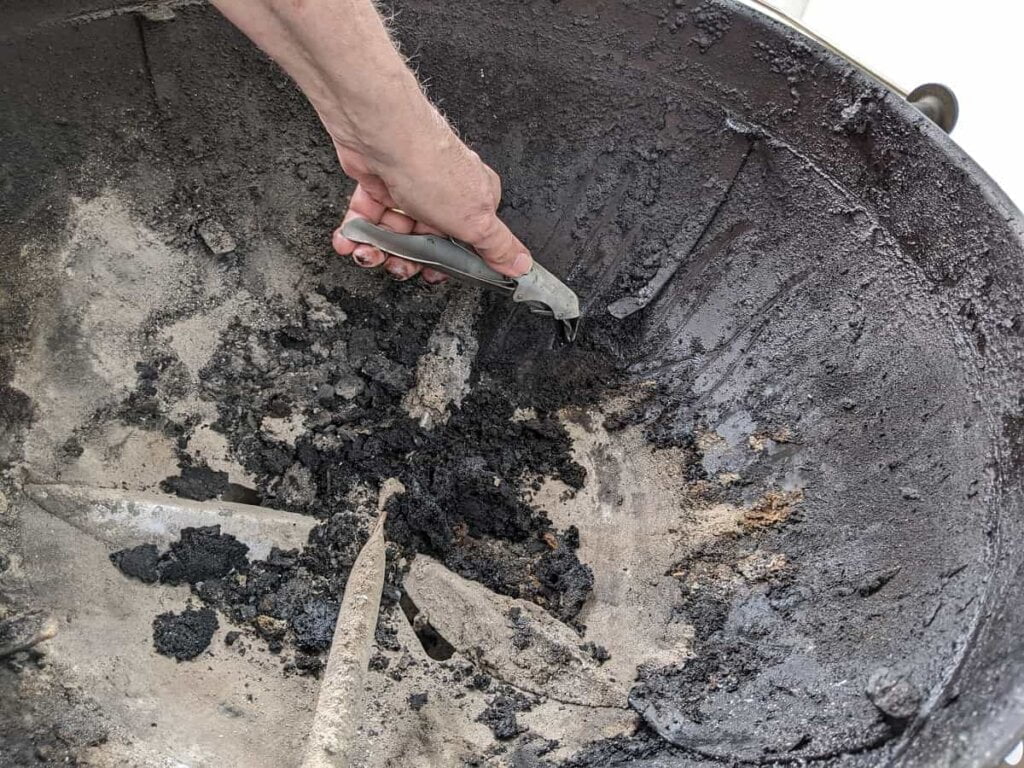 Scraping off large debris from kettle interior after grilling on charcoal many times