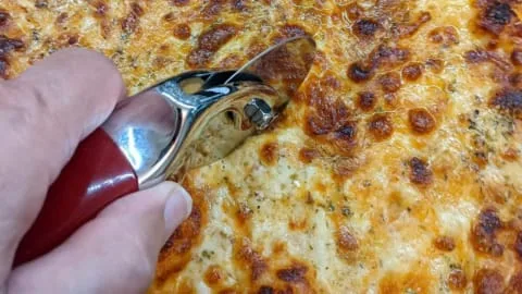 slicing homemade pizza with pizza wheel cutter