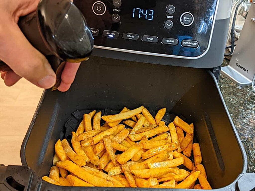 spraying oil lightly over frozen french fries in air fryer