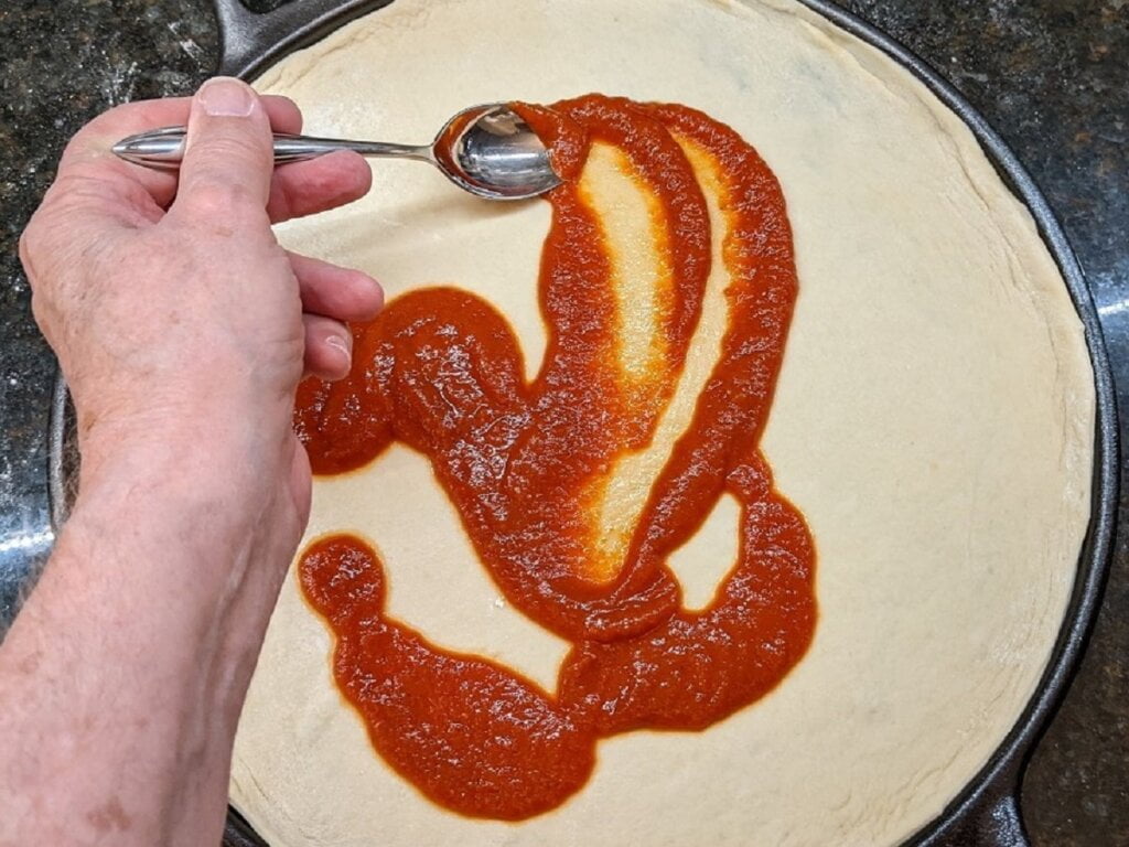 Spread pizza sauce onto dough of cast iron pizzas