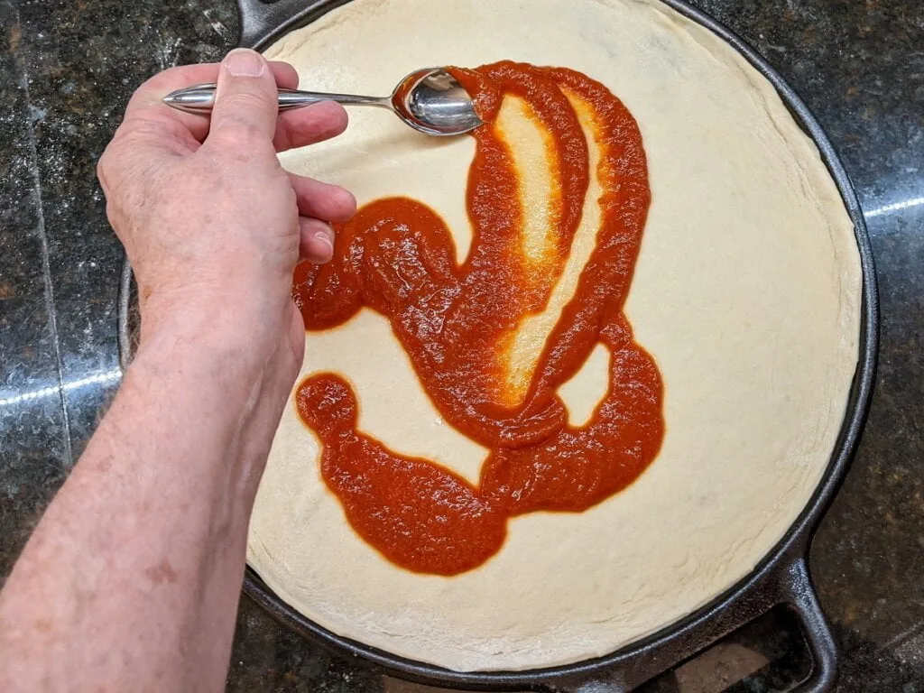 Spreading pizza sauce on dough in pizza cast iron pan