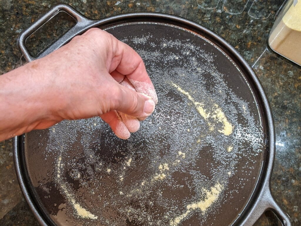 Sprinkling corn meal on oil coated surface for cast iron pizzas