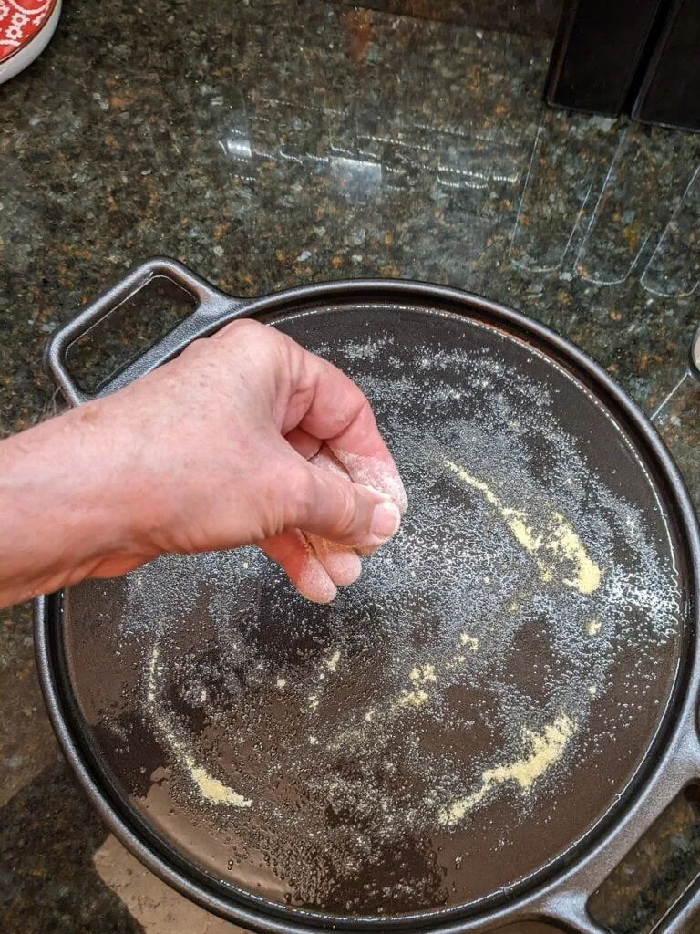Sprinkling corn meal on the oil coated pizza cast iron pan