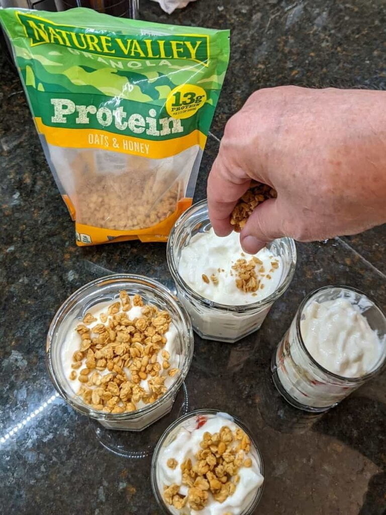 Sprinkling granola on strawberry yogurt granola parfait