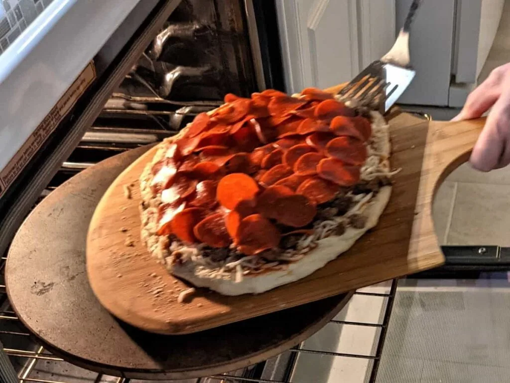 transferring pepperoni pizza from wooden peel onto pizza stone