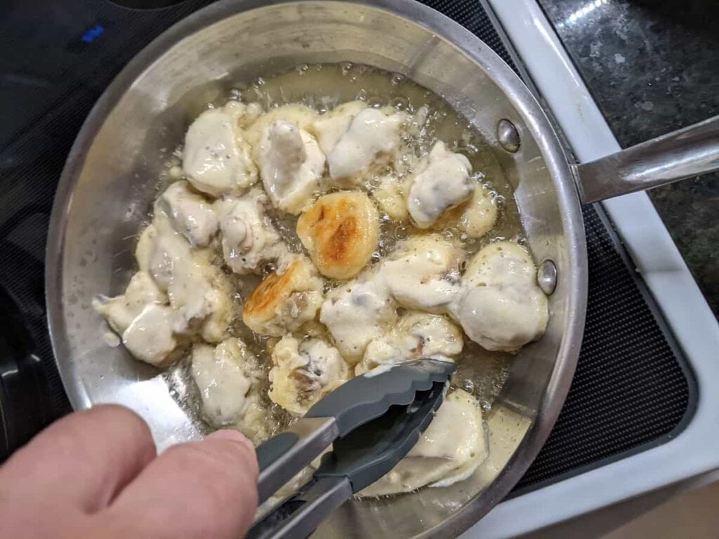 turning fried mushrooms with tongs in skillet