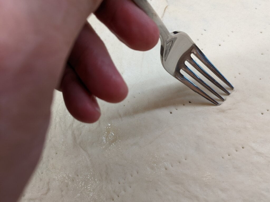 Use a fork to prick cast iron pizzas dough to reduce large bubbles during baking