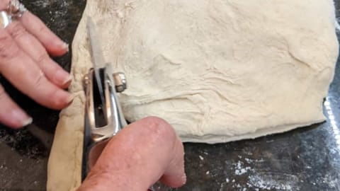 using a pizza wheel cutter to trim excess dough from calzone