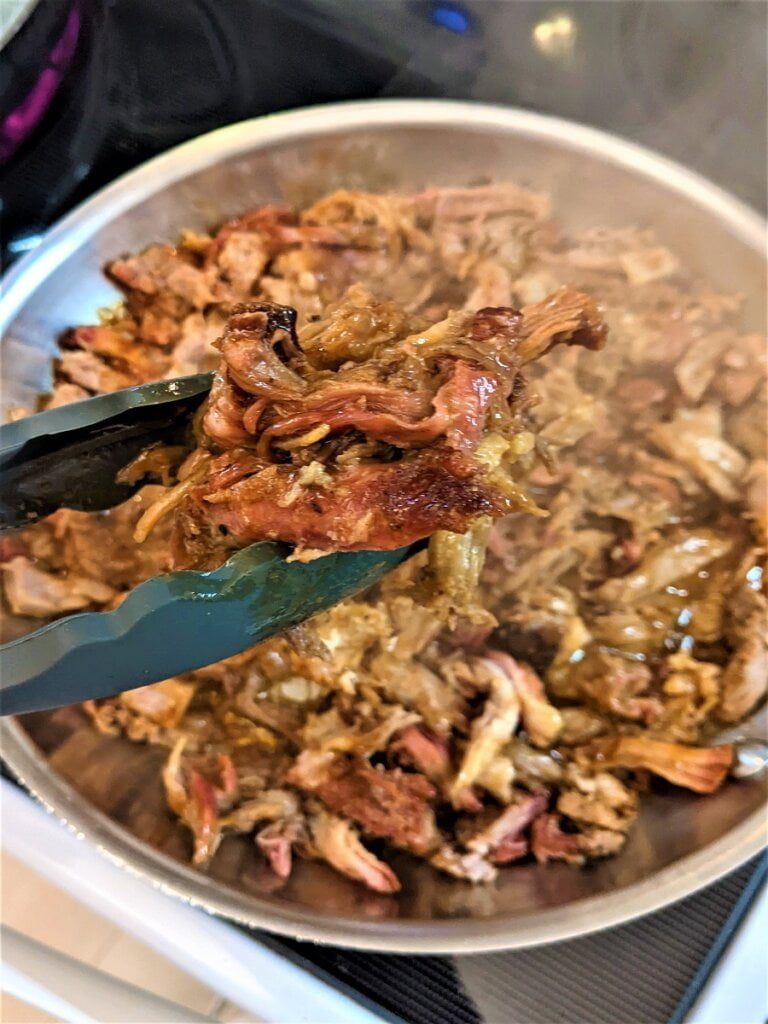 using tongs to grab pulled pork for a sandwich