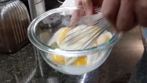 whipping egg mixture until frothy for scrambled eggs recipe in stainless steel pan